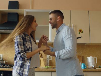 Attractive young joyful couple have fun dancing while cooking in the kitchen at home in the morining