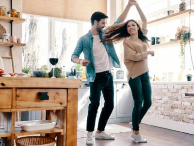 Full length of beautiful young couple in casual clothing dancing and smiling while standing in the kitchen at home